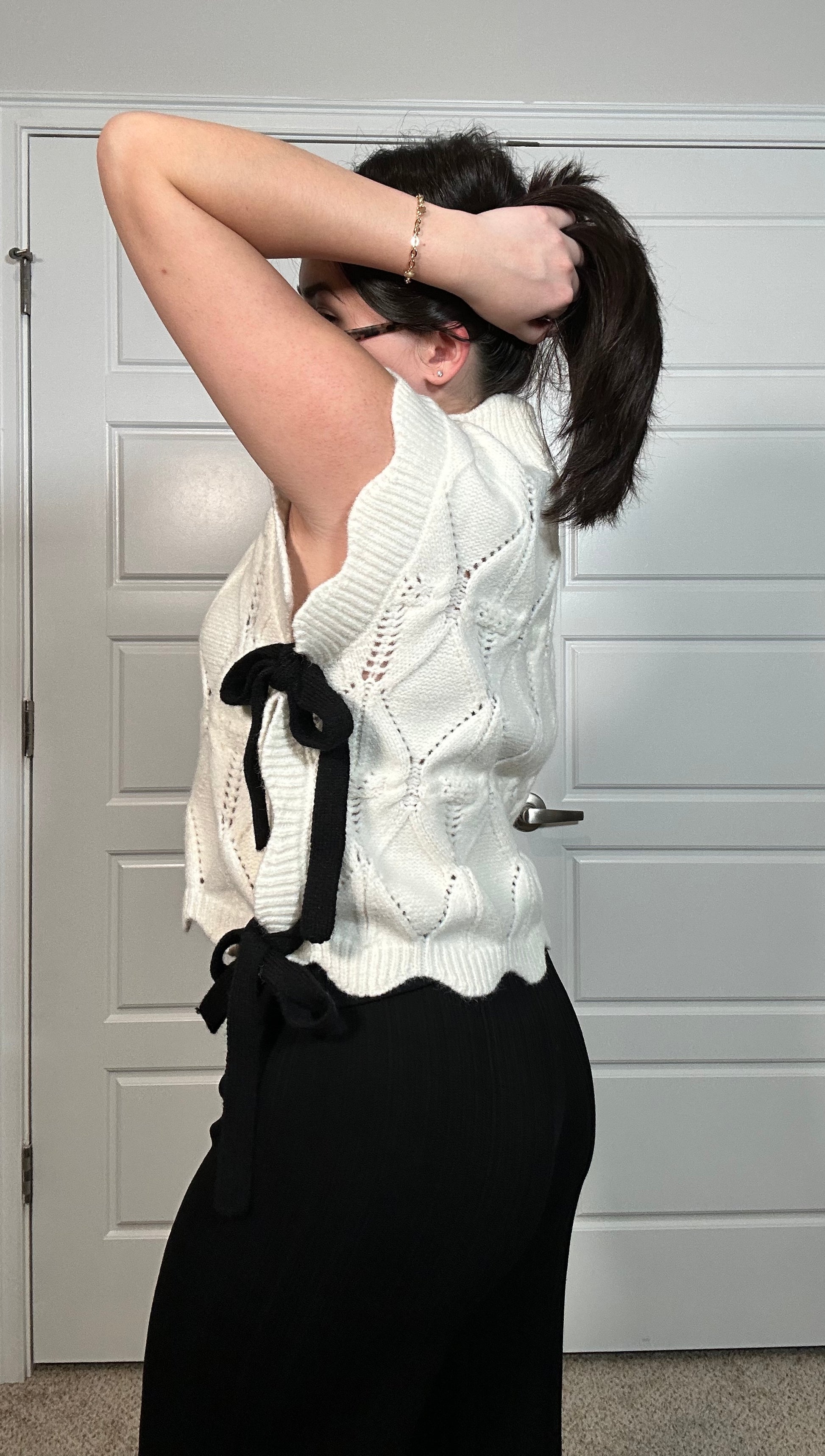 White sweater vest with scalloped detail and black bow on the side