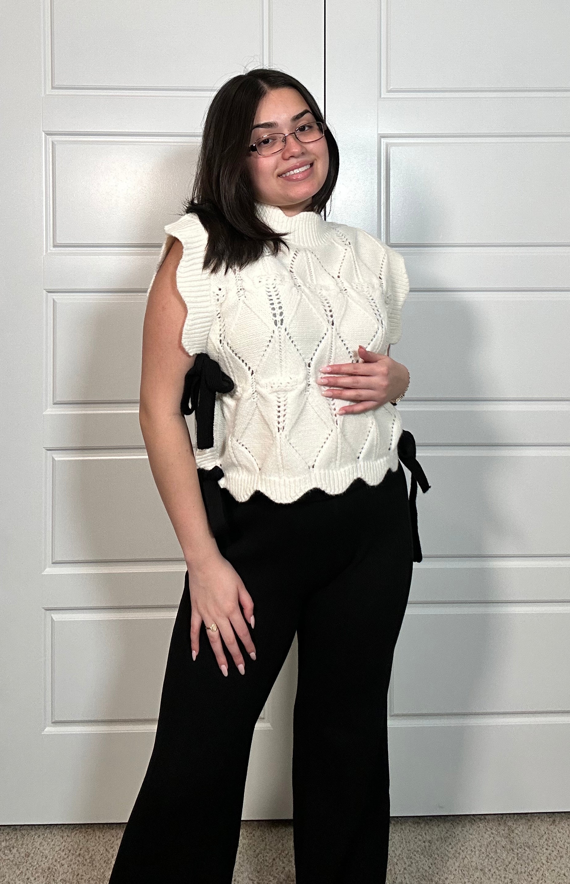 White sweater vest with scalloped detail and black bow on the side